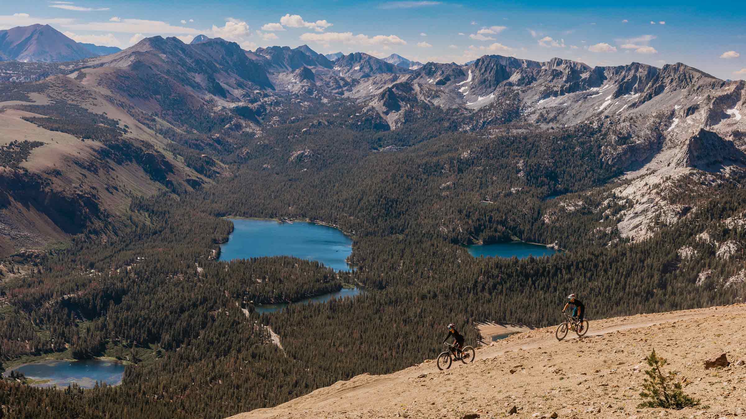 Two mountain bikers riding Off the Top with a view of the Lakes Basin.